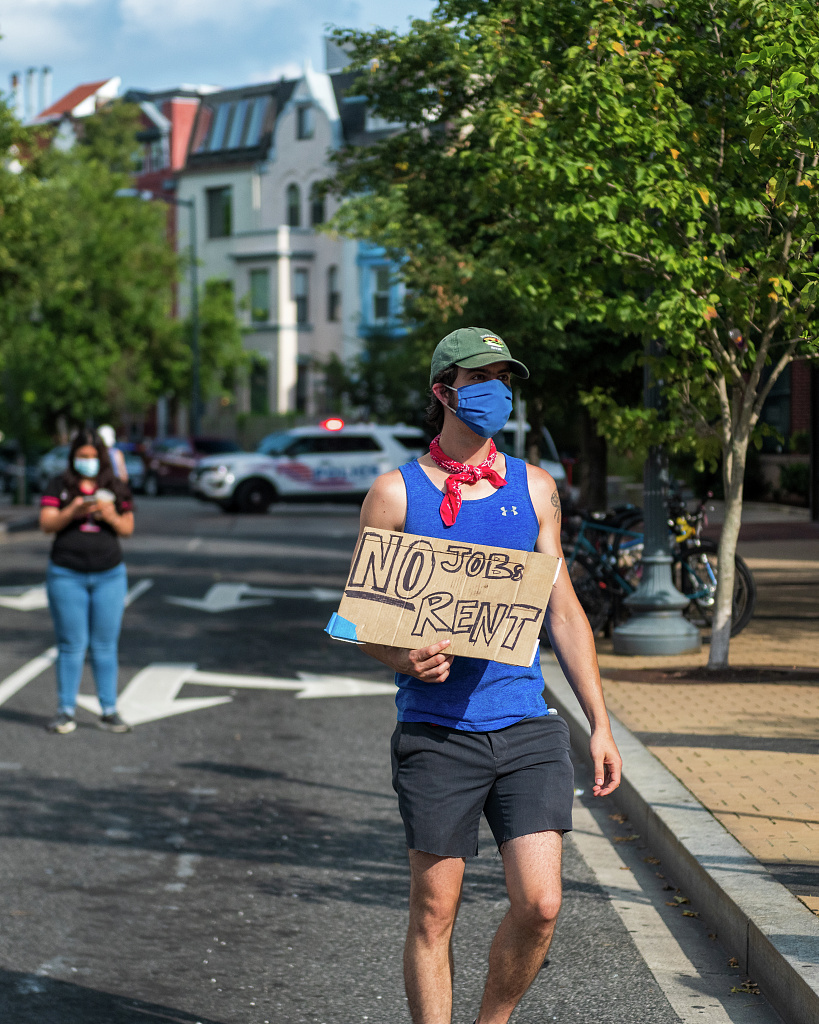 A rent strike protestor holding a sign that reads "NO jobs, NO rent."